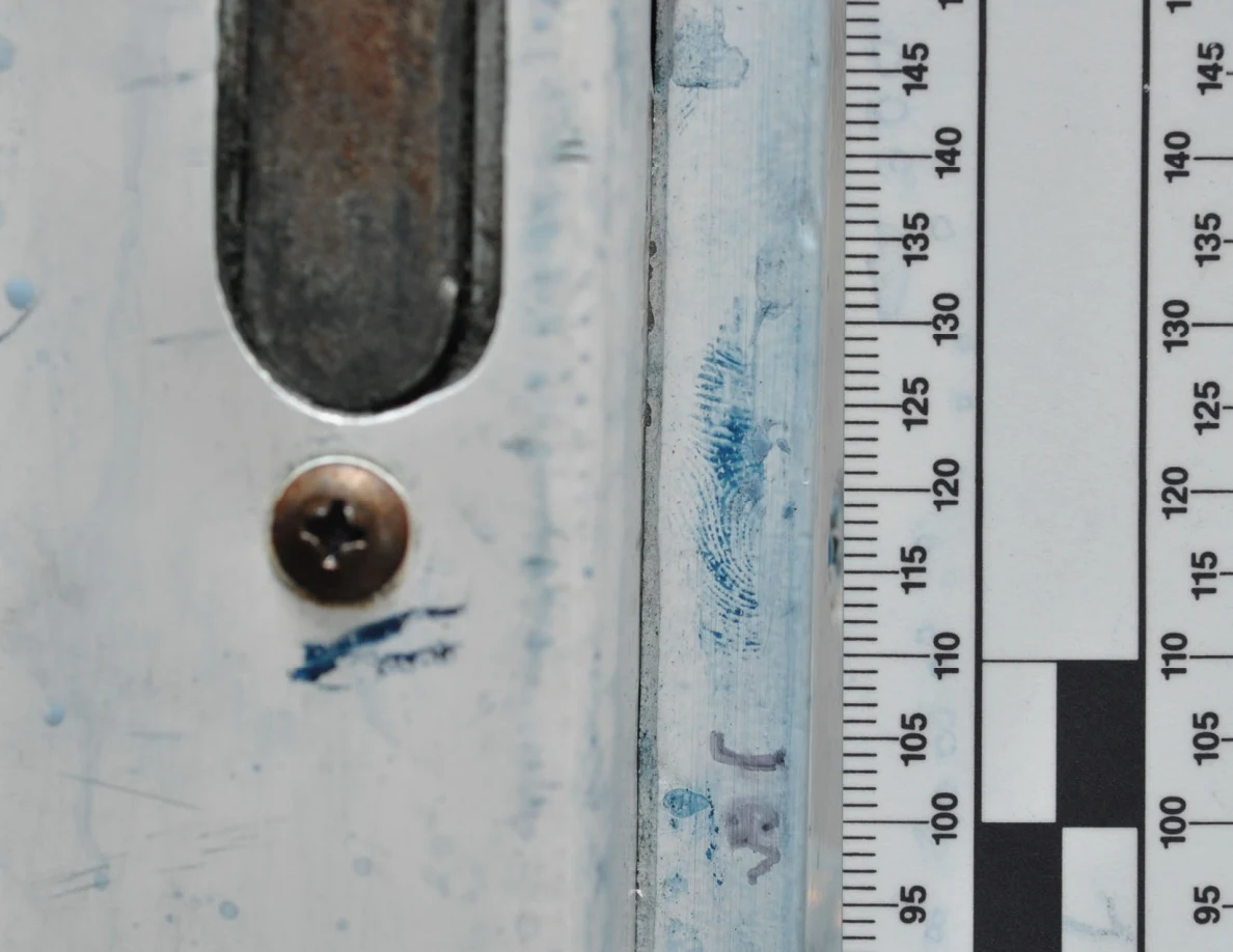 Close view of door latch, screw and blue ridge-pattern marks beside a ruler.