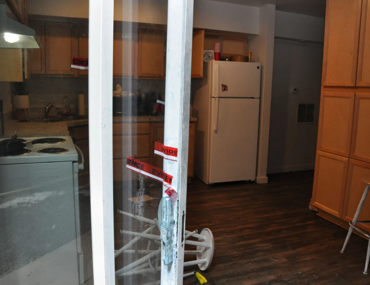 Kitchen refrigerator, stove and wooden cabinets seen through a sliding door with red evidence tape.