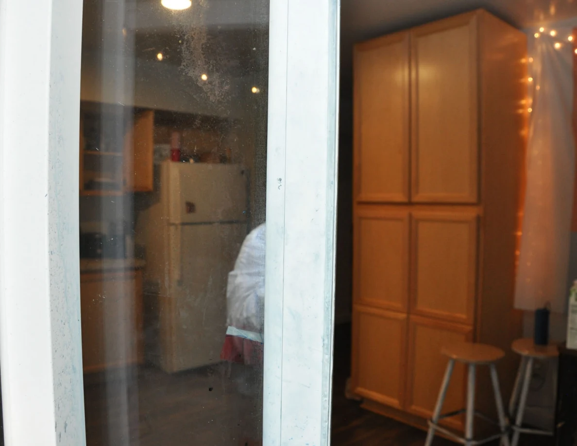 Sliding-door frame in front of wooden cabinets and stools, with a reflected figure in protective coveralls.