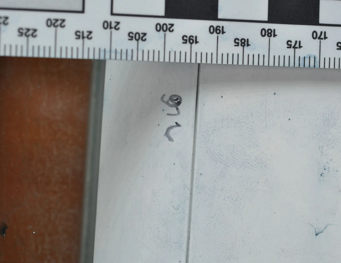 Close view of a white door frame with faint blue marks and handwriting beneath a measurement scale.
