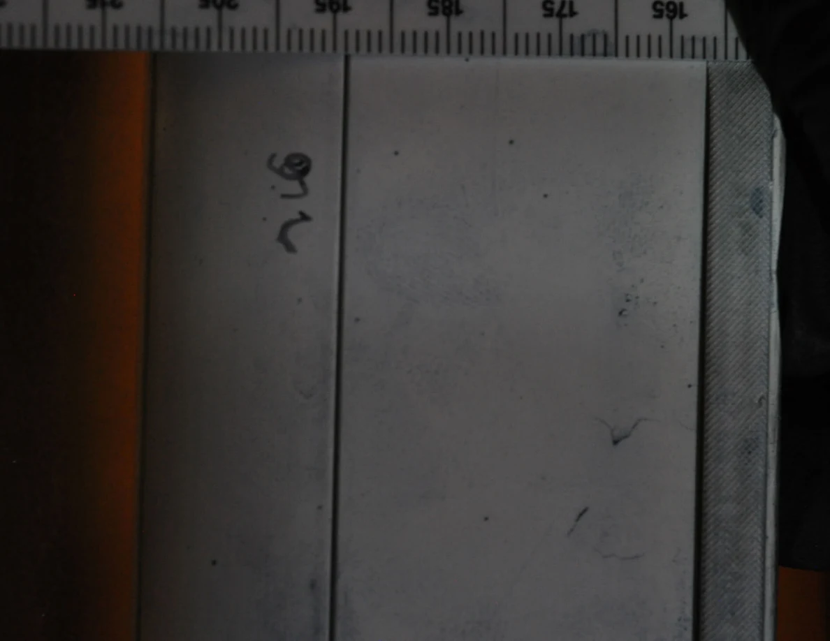 Dim close view of faint blue marks on a white frame beside a measurement scale.