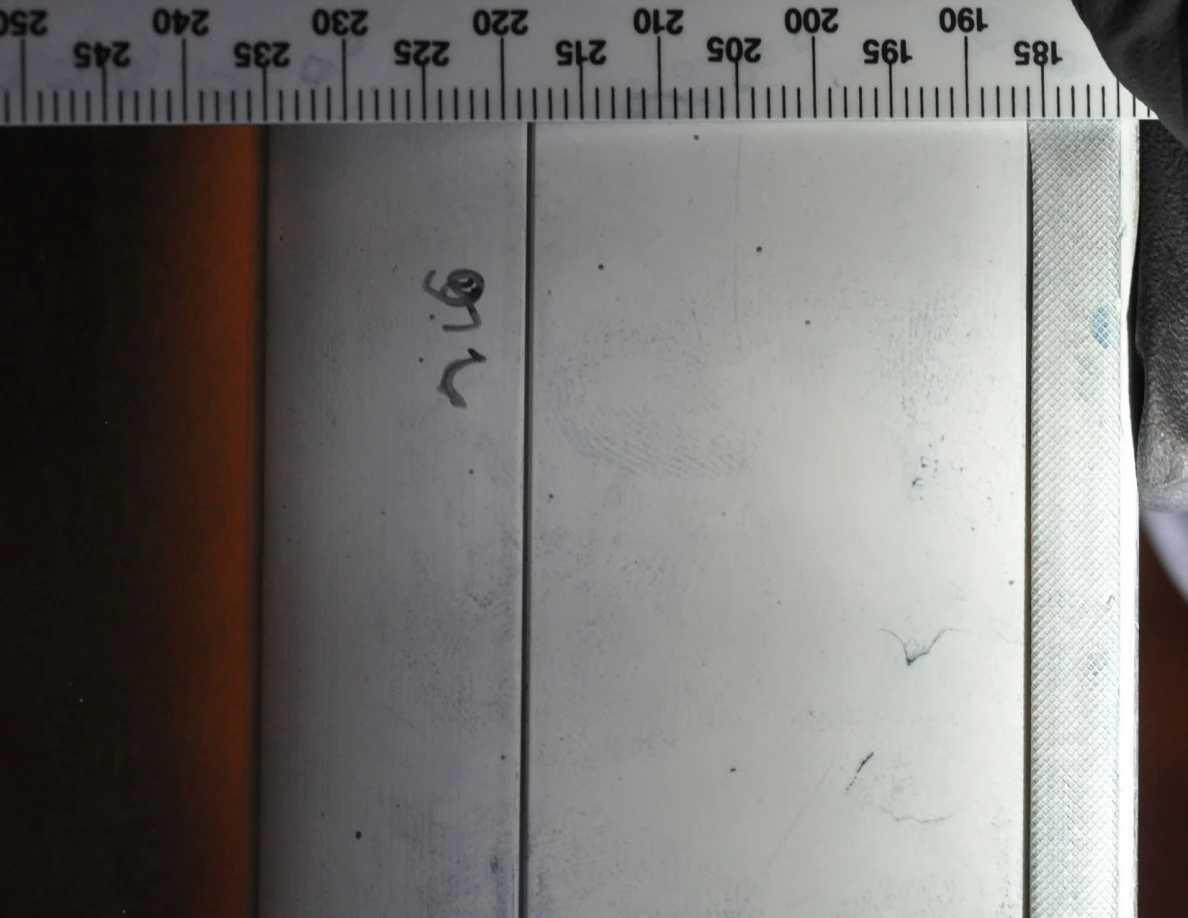 White frame with faint blue ridge-pattern marks and handwritten notation beside a scale.