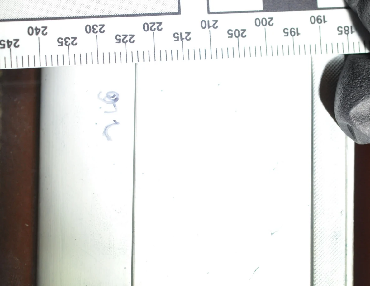 Close view of a white frame and faint blue marks with a ruler held along its edge.