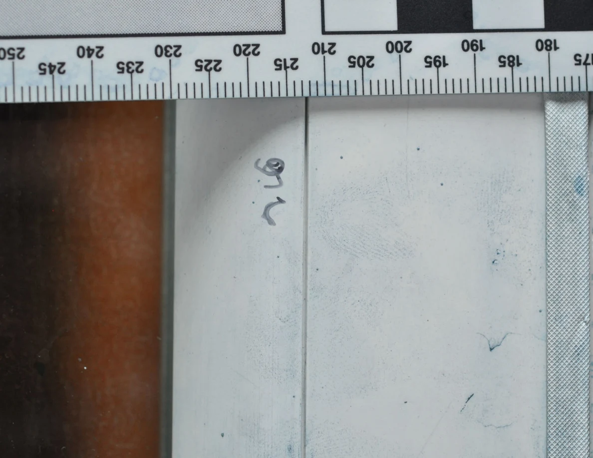 White door-frame surface with faint blue ridge-pattern marks and handwriting beside a ruler.