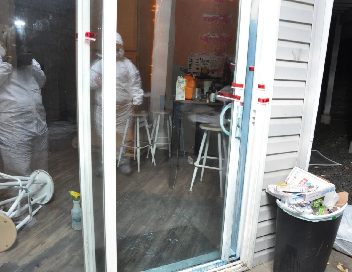Sliding glass doorway with blue marks, red evidence tape, kitchen stools and reflections of people in protective coveralls.