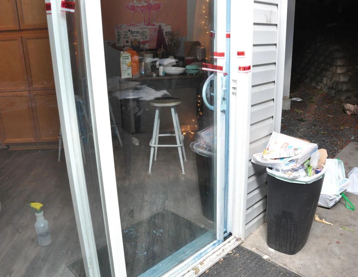 Sliding glass door beside an overflowing black trash bin, with table and stools visible inside.