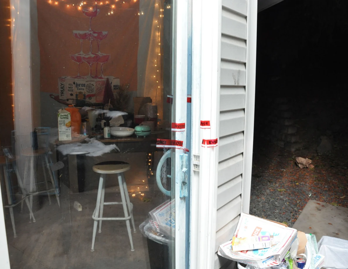 Close view of sliding-door handle and red evidence tape, with dining table and string lights beyond.