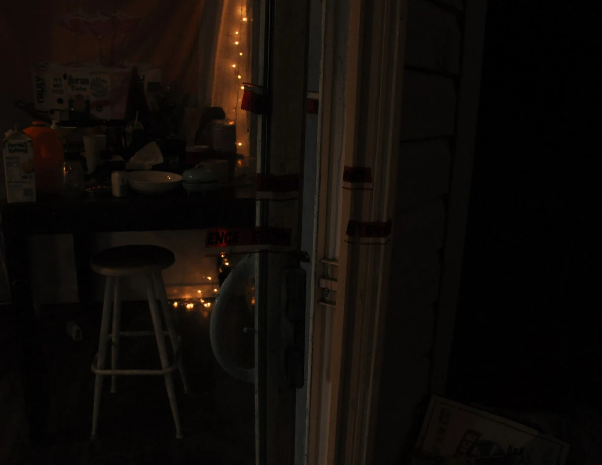 Dim view of sliding-door frame beside dining table, stools and decorative string lights.