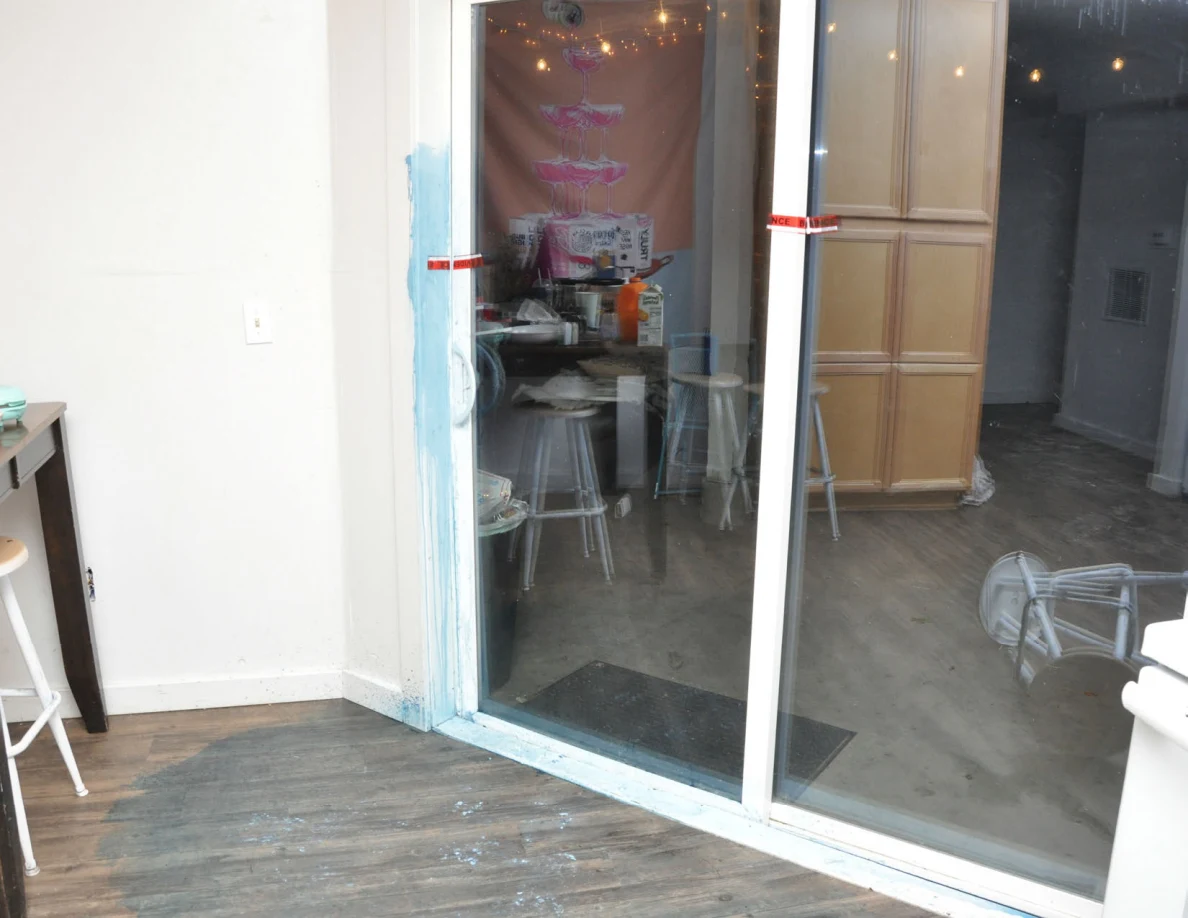 Interior view of a closed sliding glass door with blue residue on its frame and stools reflected in the glass.
