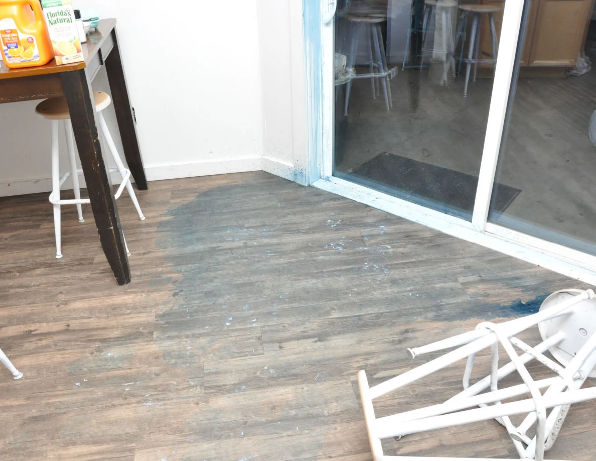 Wood-look floor beside sliding door, with blue residue and an overturned white stool.