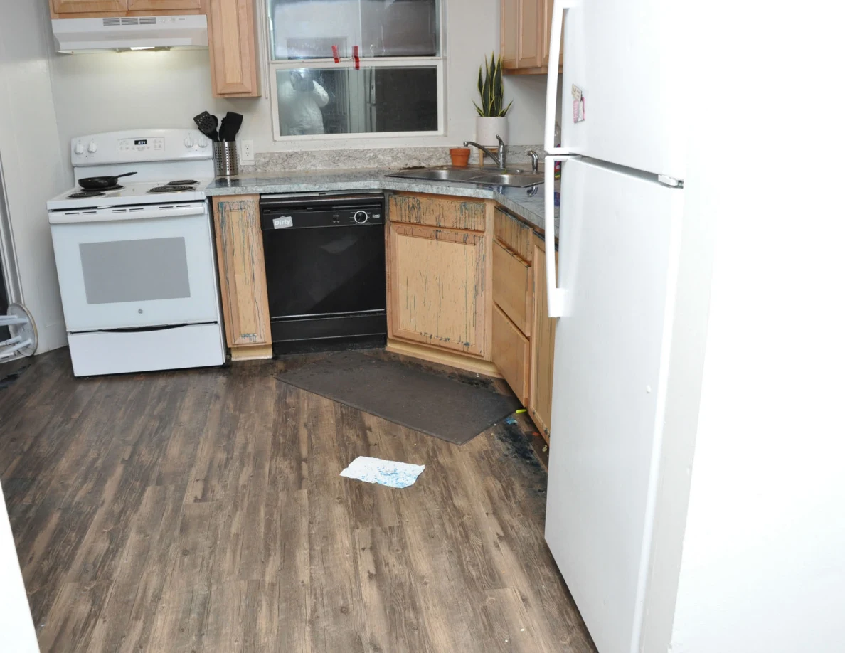 Kitchen with white stove and refrigerator, black dishwasher, wooden cabinets and a paper on the floor.