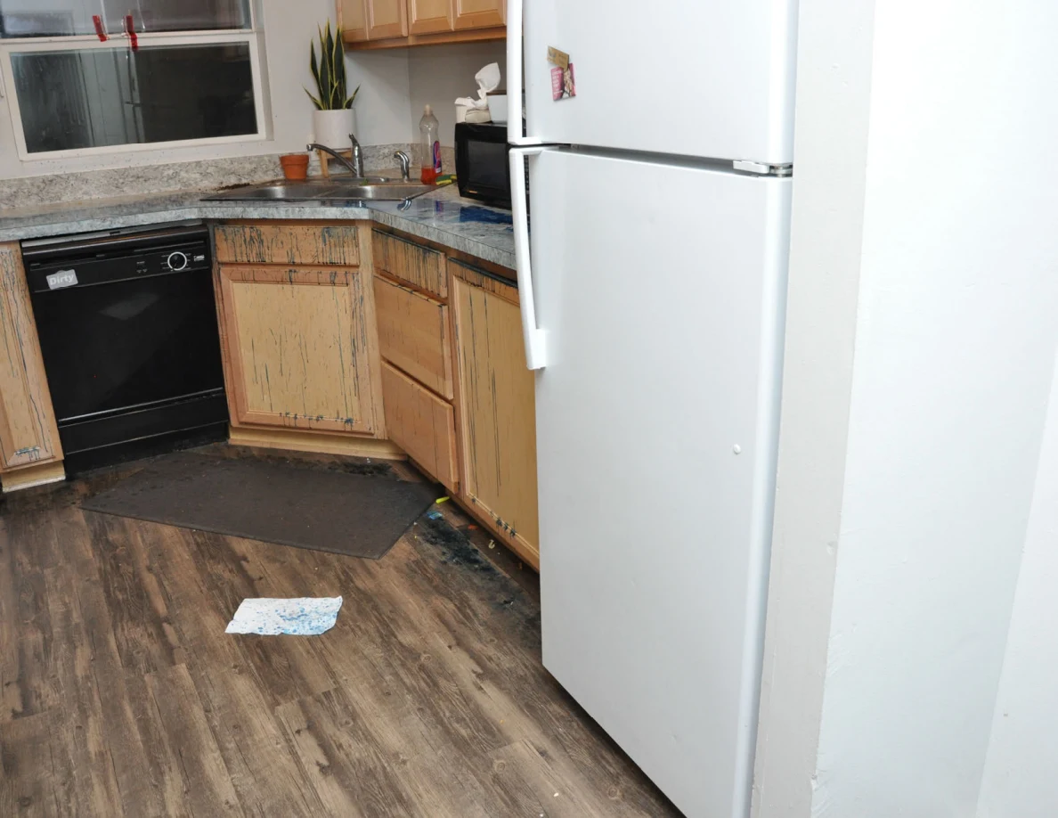 White refrigerator beside wooden kitchen cabinets, black dishwasher and a paper on wood-look flooring.
