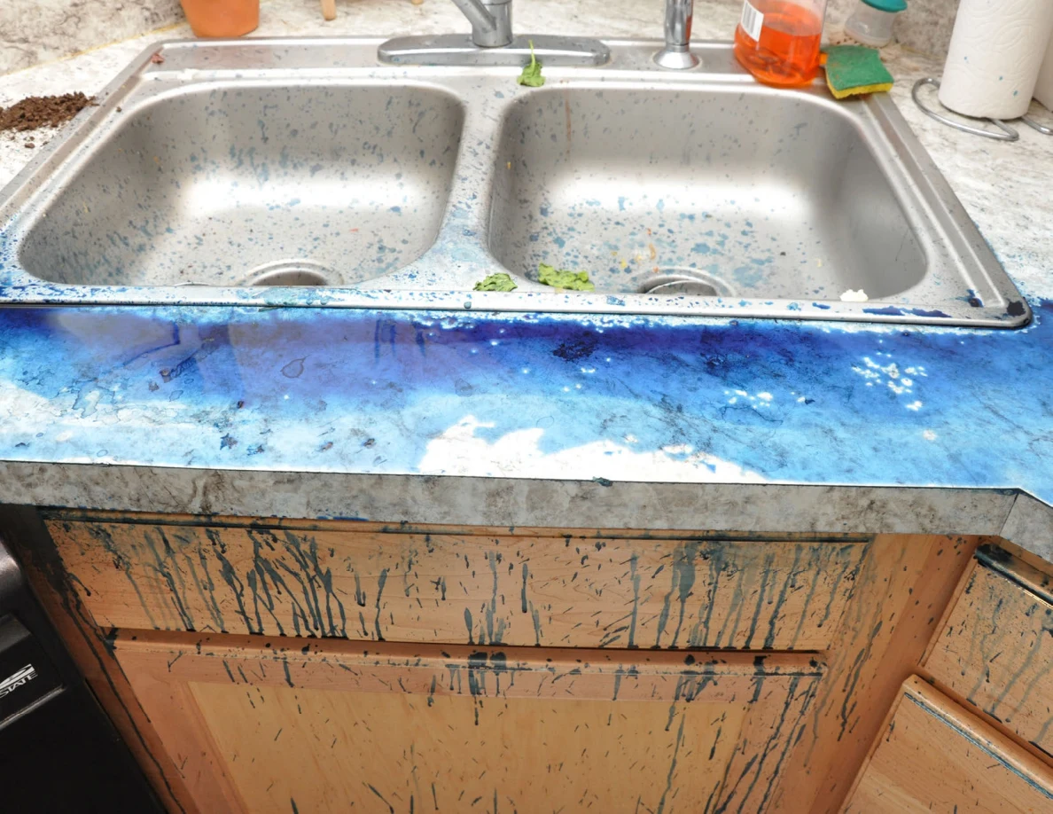 Double stainless-steel sink with blue specks and broad blue residue on the surrounding counter.