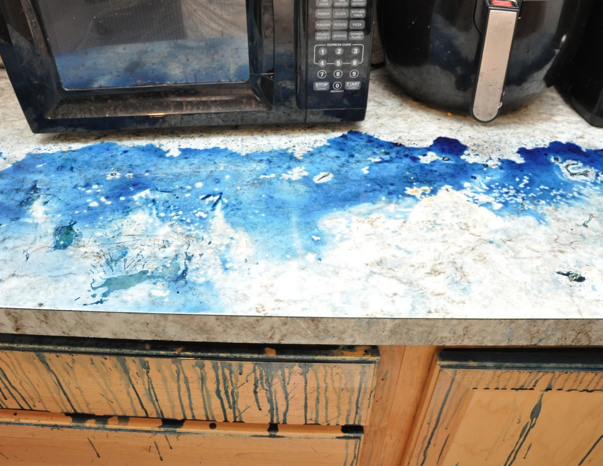 Bright view of blue residue on countertop beneath microwave and air fryer, with streaked drawers.