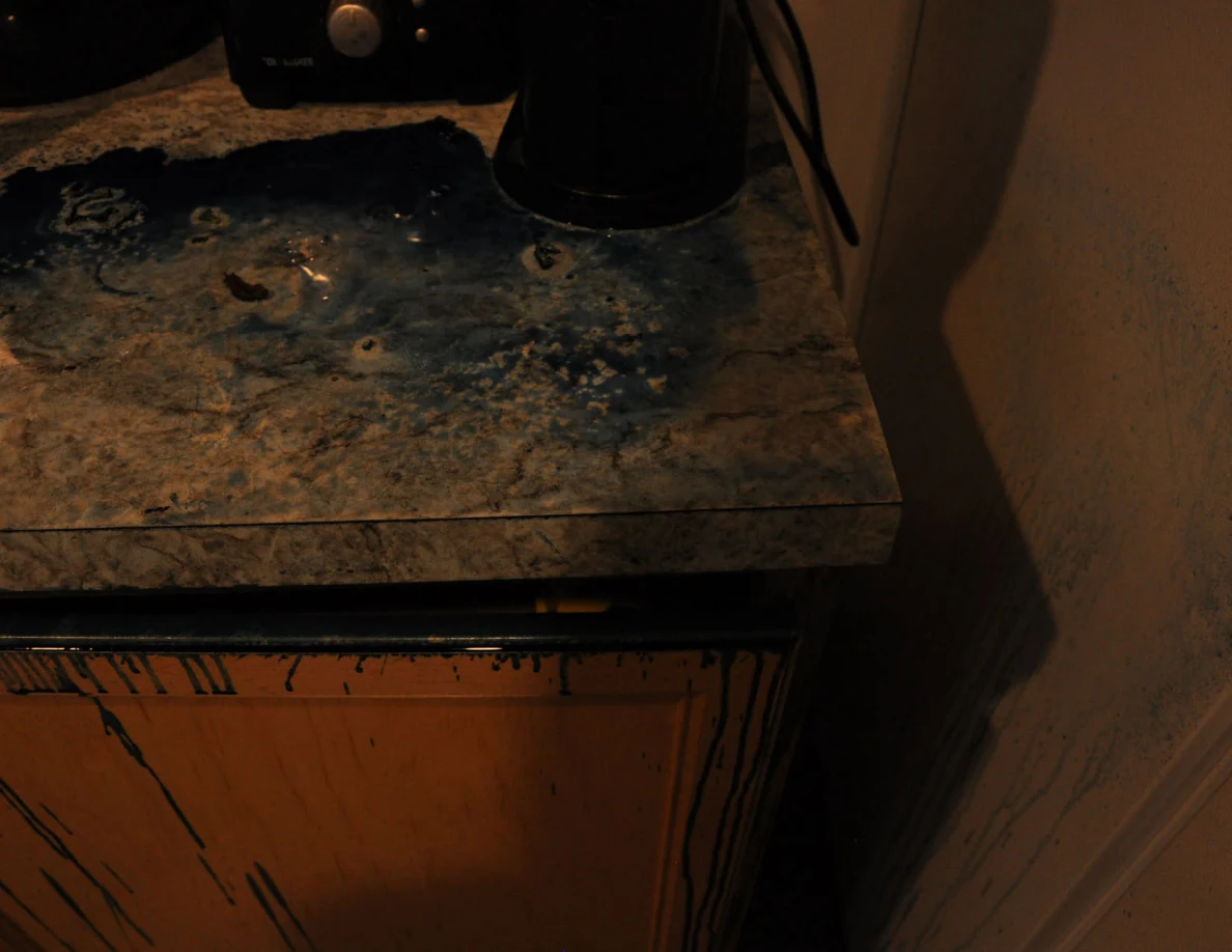 Dim view of dark blue residue on a counter corner beneath small appliances.