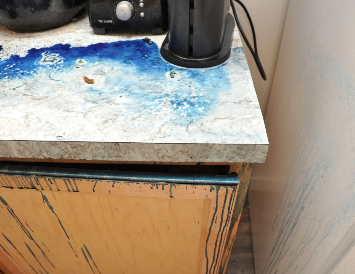 Bright view of blue residue on a counter corner beside a small black appliance and white wall.