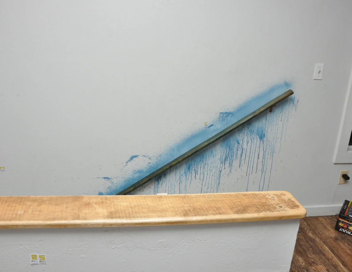 Wooden stair handrail with blue residue on the wall around it, behind a wood-capped half-wall.