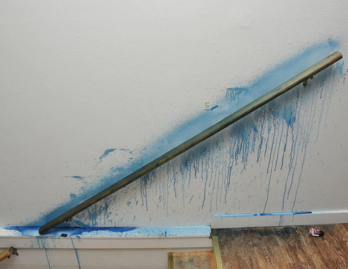 Blue streaks on a pale wall beneath a stair handrail.