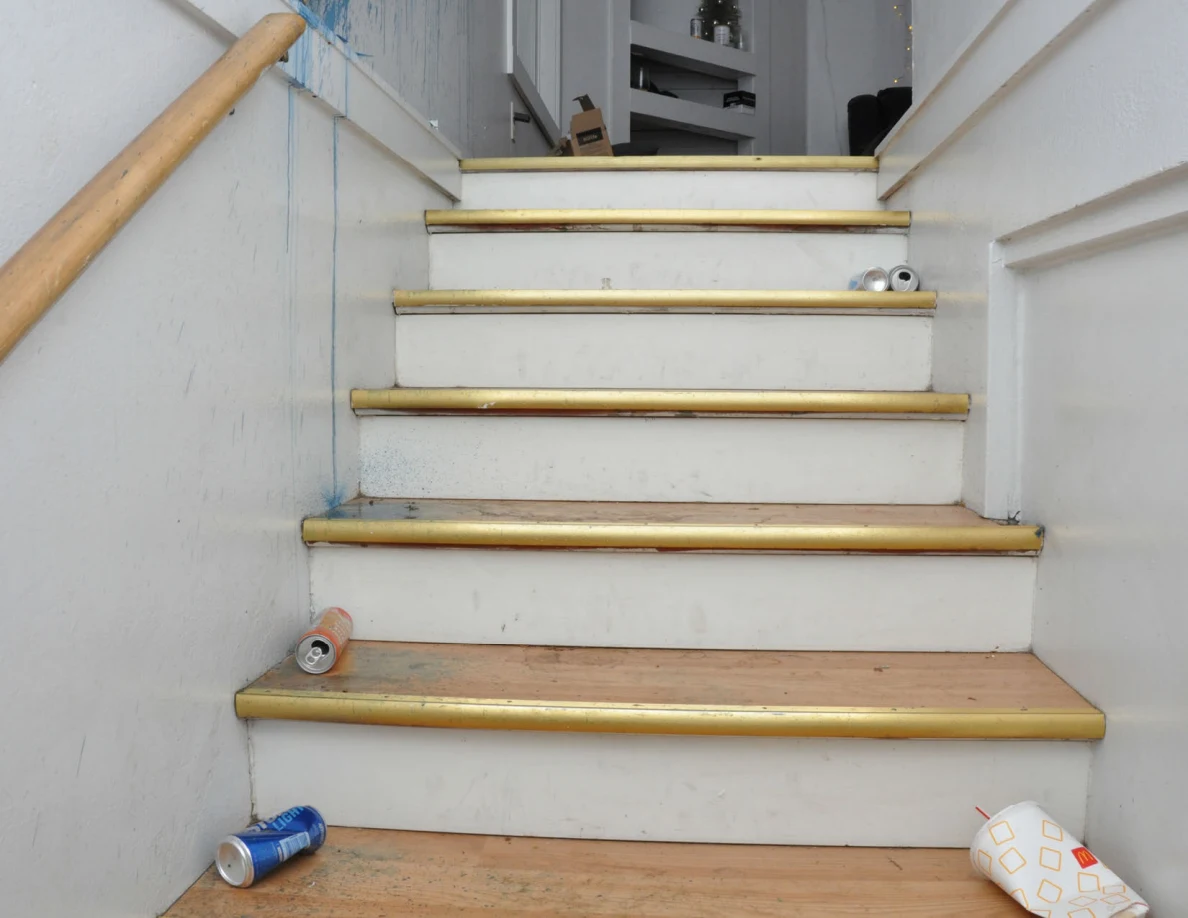 Wooden stairs with white risers and metal edges, with drink cans and a paper cup on several steps.