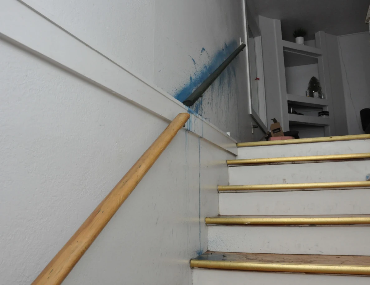 View up stairs beside a wooden handrail and blue-streaked wall.