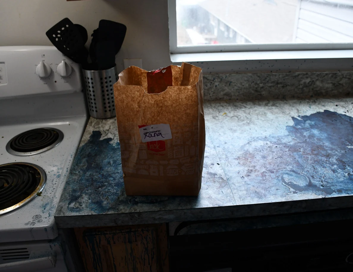 Brown takeout bag on a blue-marked kitchen counter beside a stove and utensil holder.