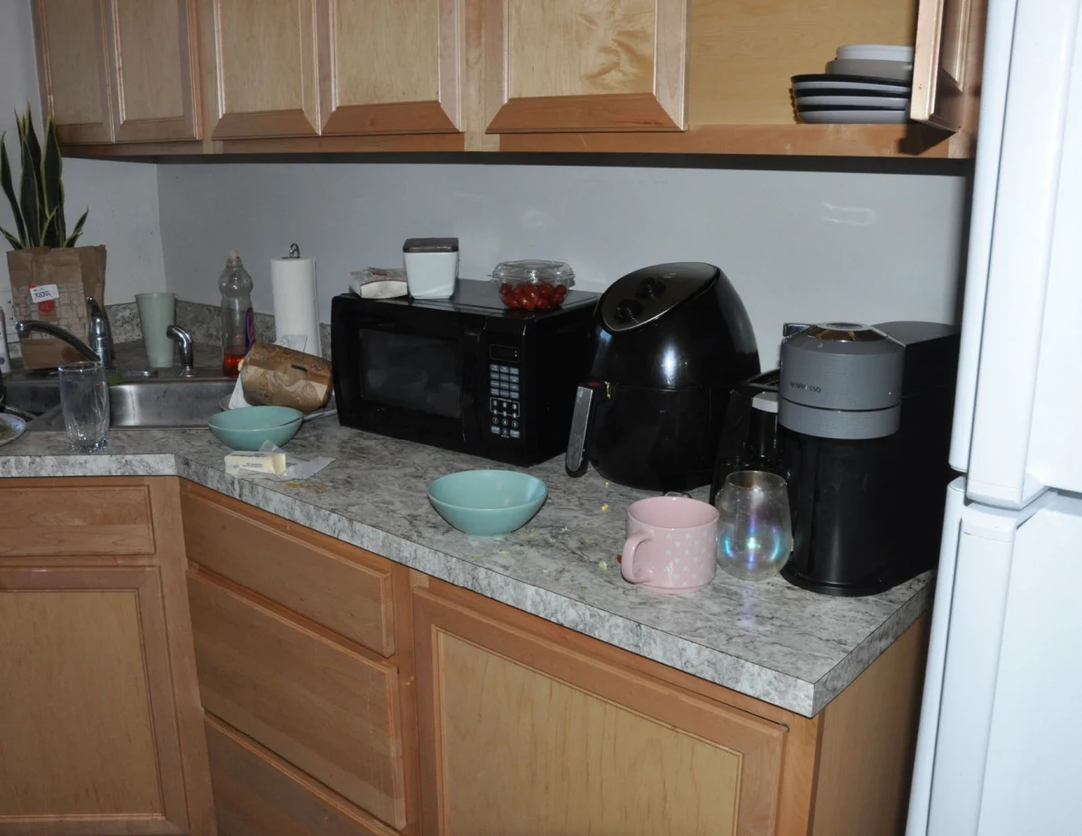 Microwave, air fryer, coffee maker, bowls and mugs on a kitchen counter beneath wooden cabinets.