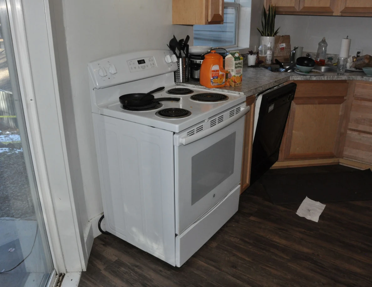 White electric stove with frying pan beside a black dishwasher and a paper on the floor.