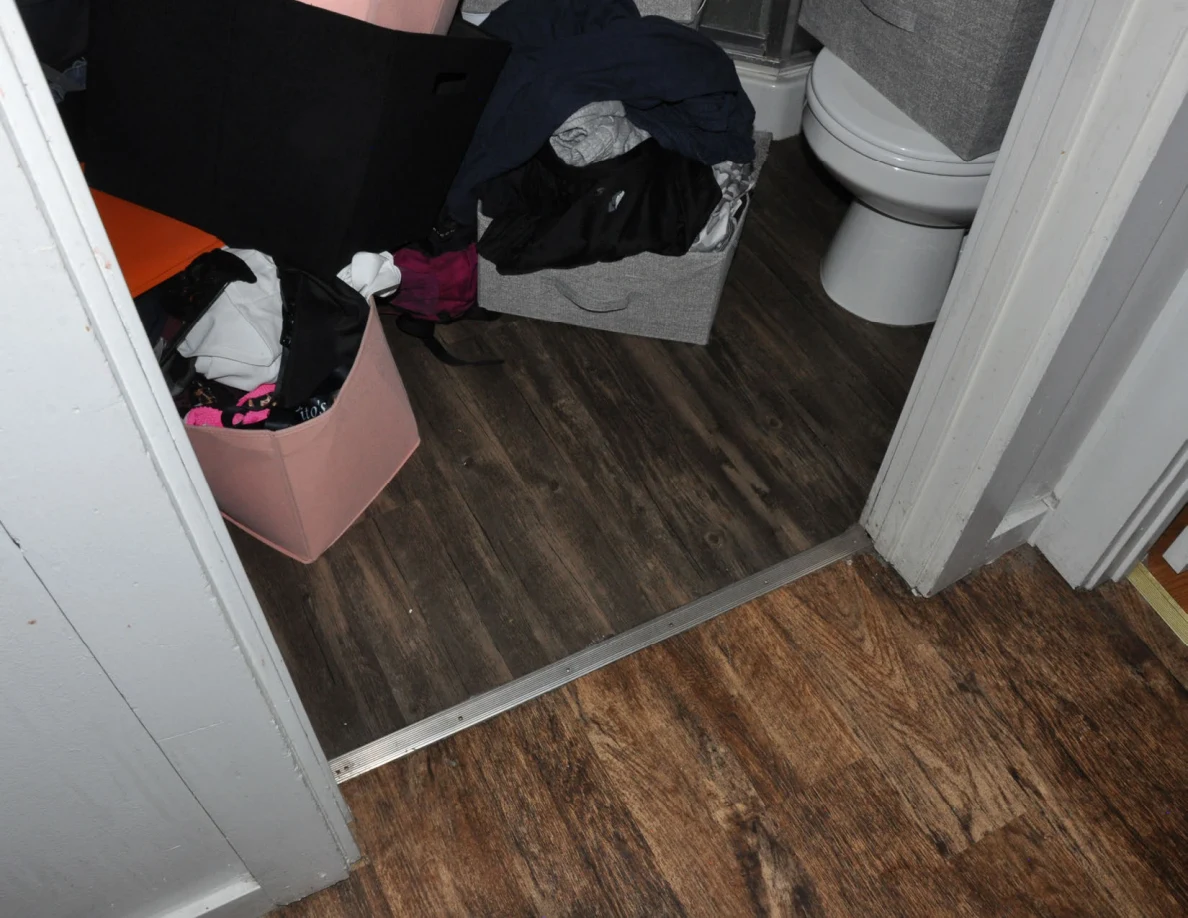 Bathroom doorway showing fabric bins filled with clothing beside a toilet.
