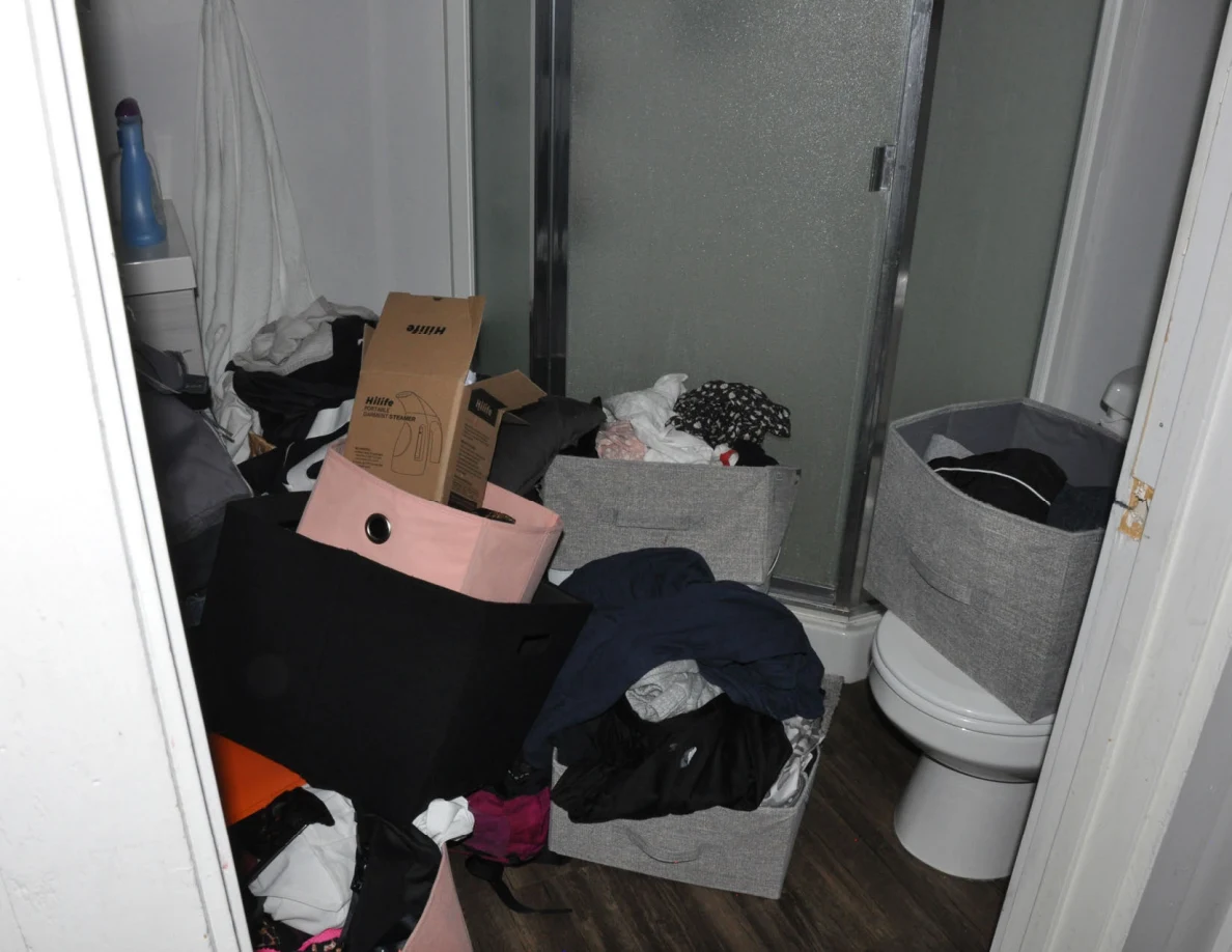 Bathroom with clothing-filled bins, bags and boxes in front of a frosted-glass shower.