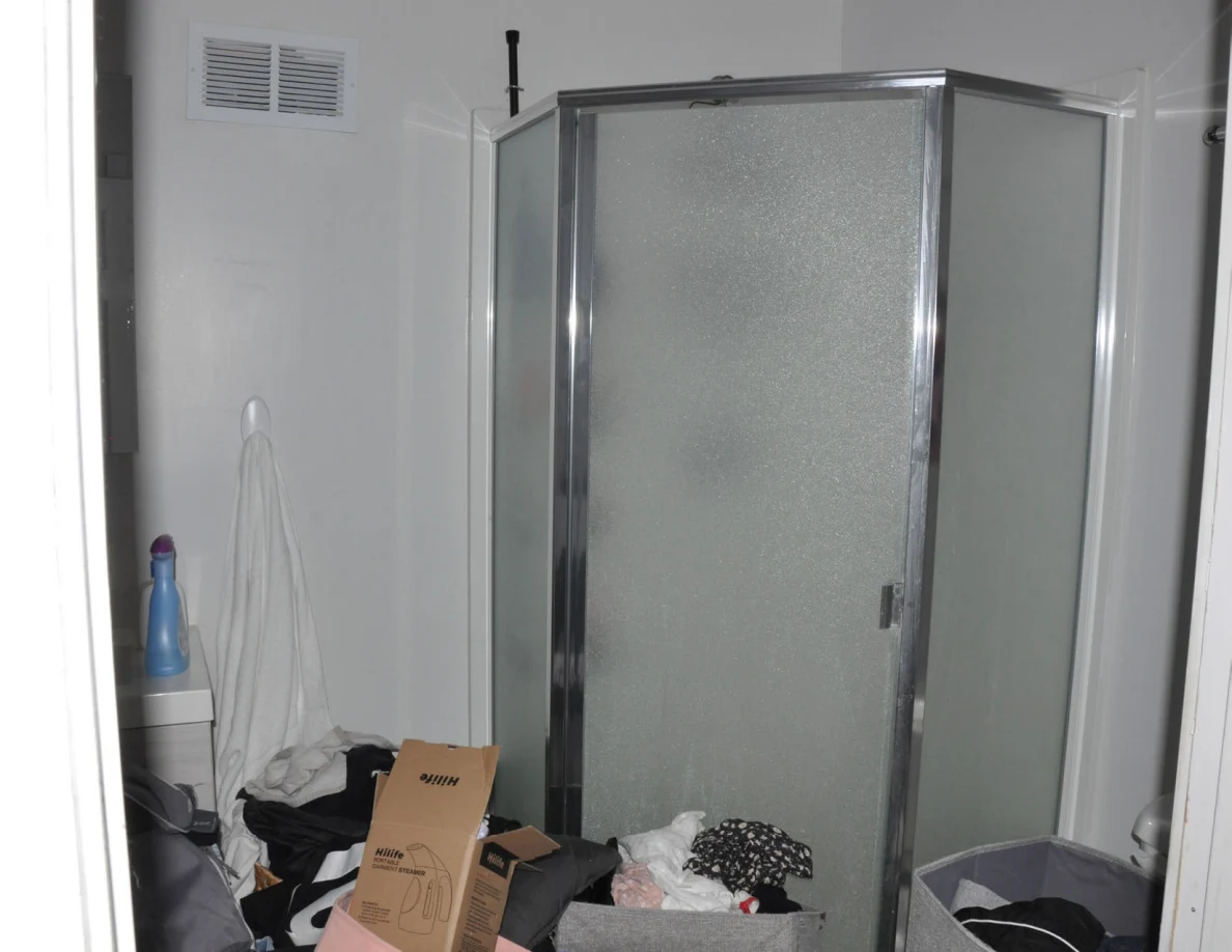 Frosted-glass shower enclosure above crowded clothing bins and boxes.