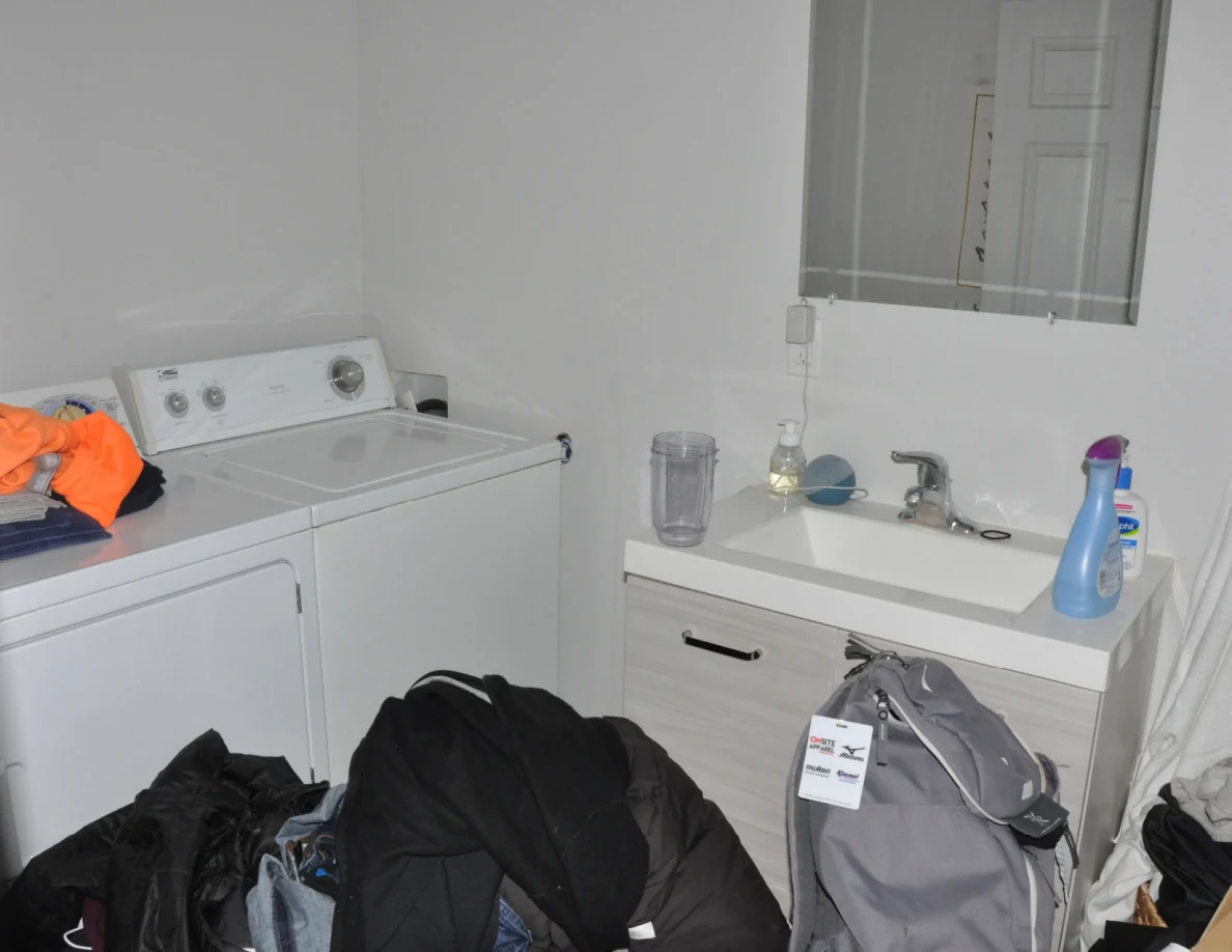 White washer and dryer beside sink vanity, with clothing piles and gray backpack below.