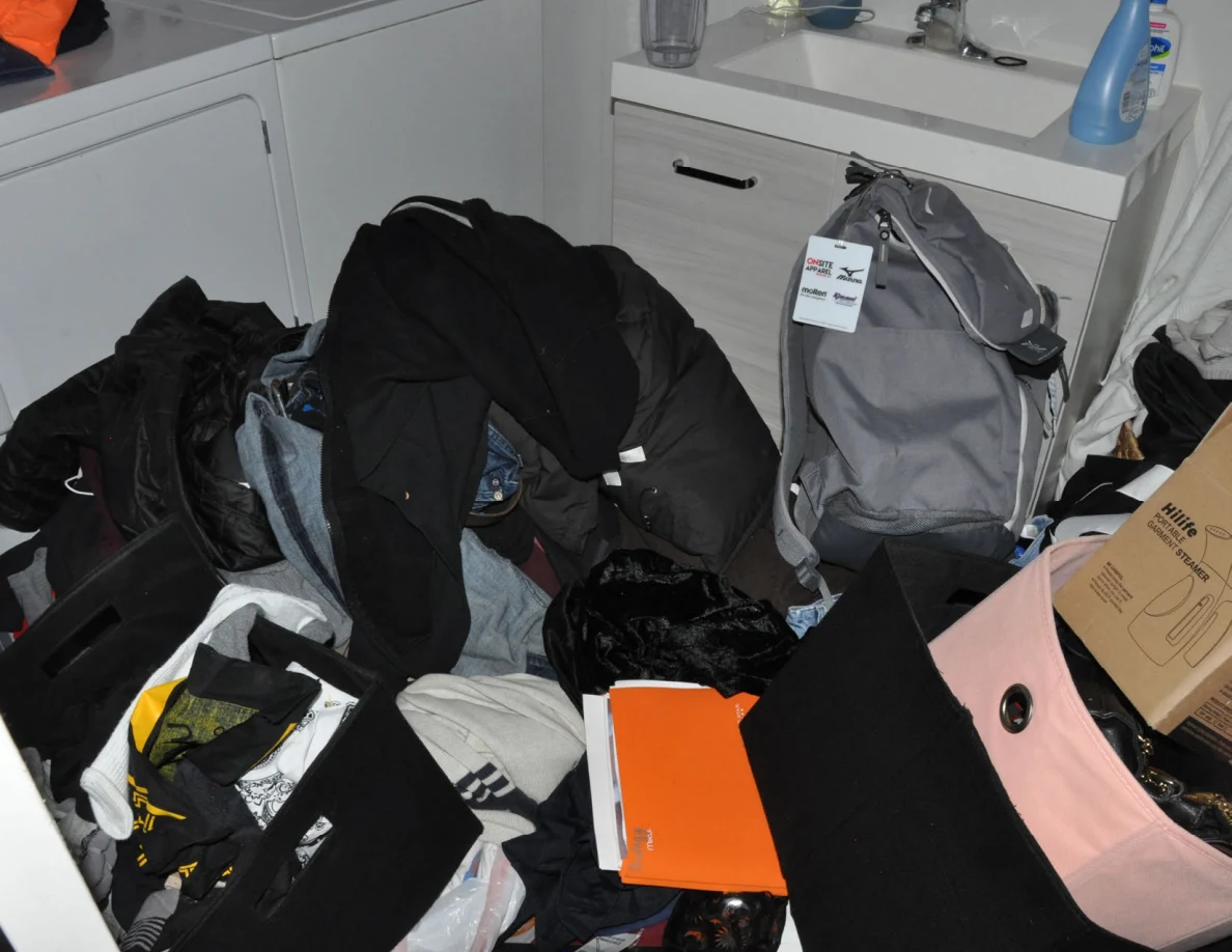 Gray backpack and clothing-filled bags and bins in front of a sink vanity.