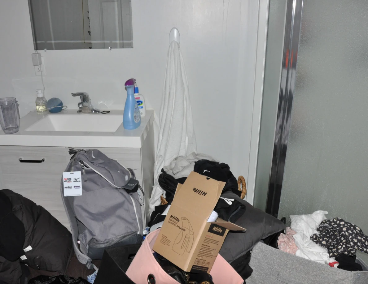 Sink vanity beside frosted-glass shower, with backpack, boxes and clothing bins in front.