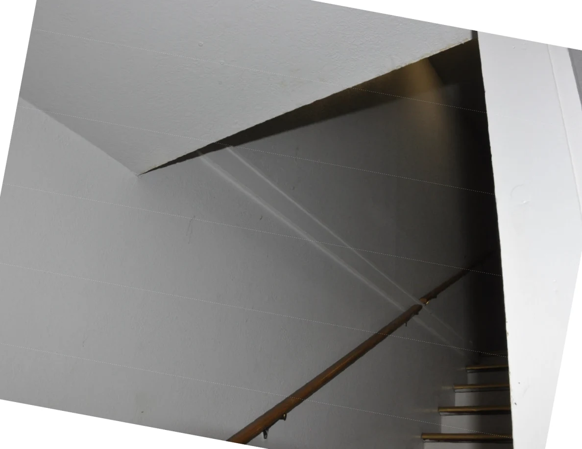 Tilted photograph of a stairwell with wooden handrail and several thin lines stretched across the space.