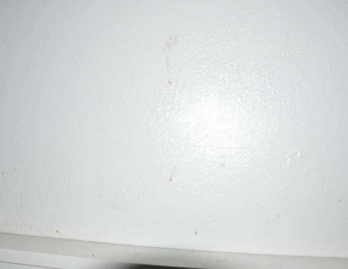 Closer view of faint reddish marks on a pale wall above white trim.