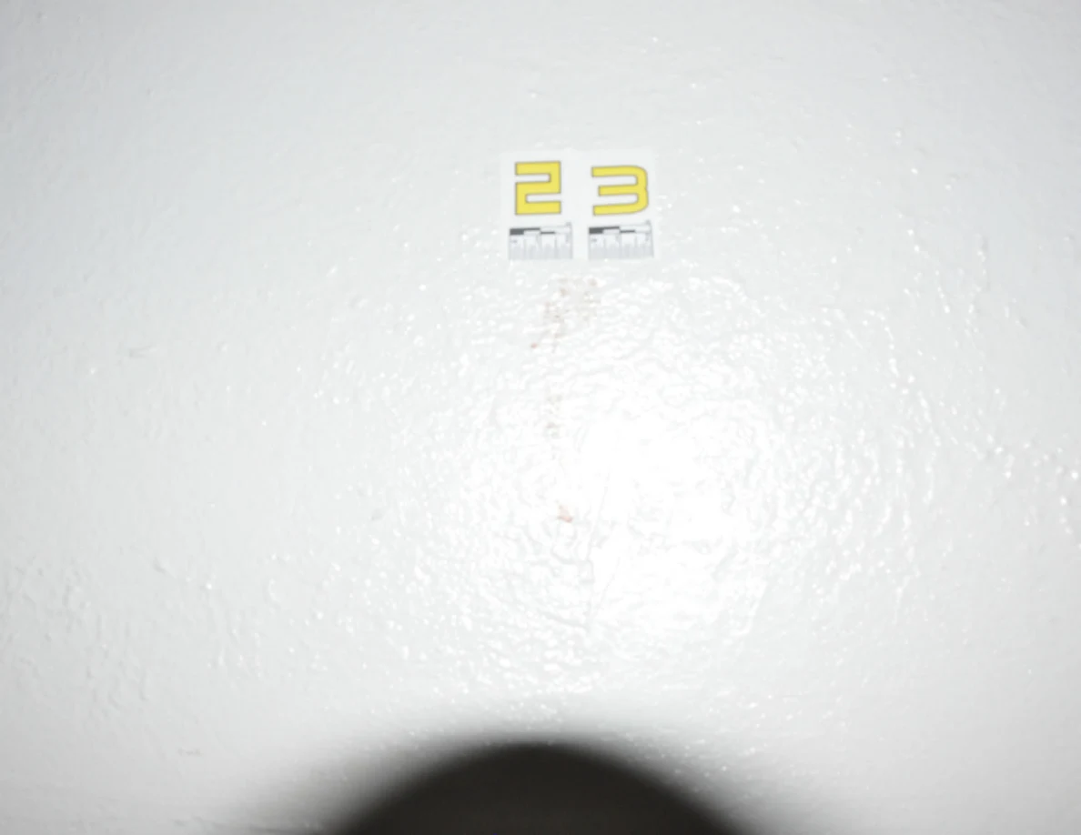 Yellow label 23 on a pale textured wall above a reddish vertical mark.