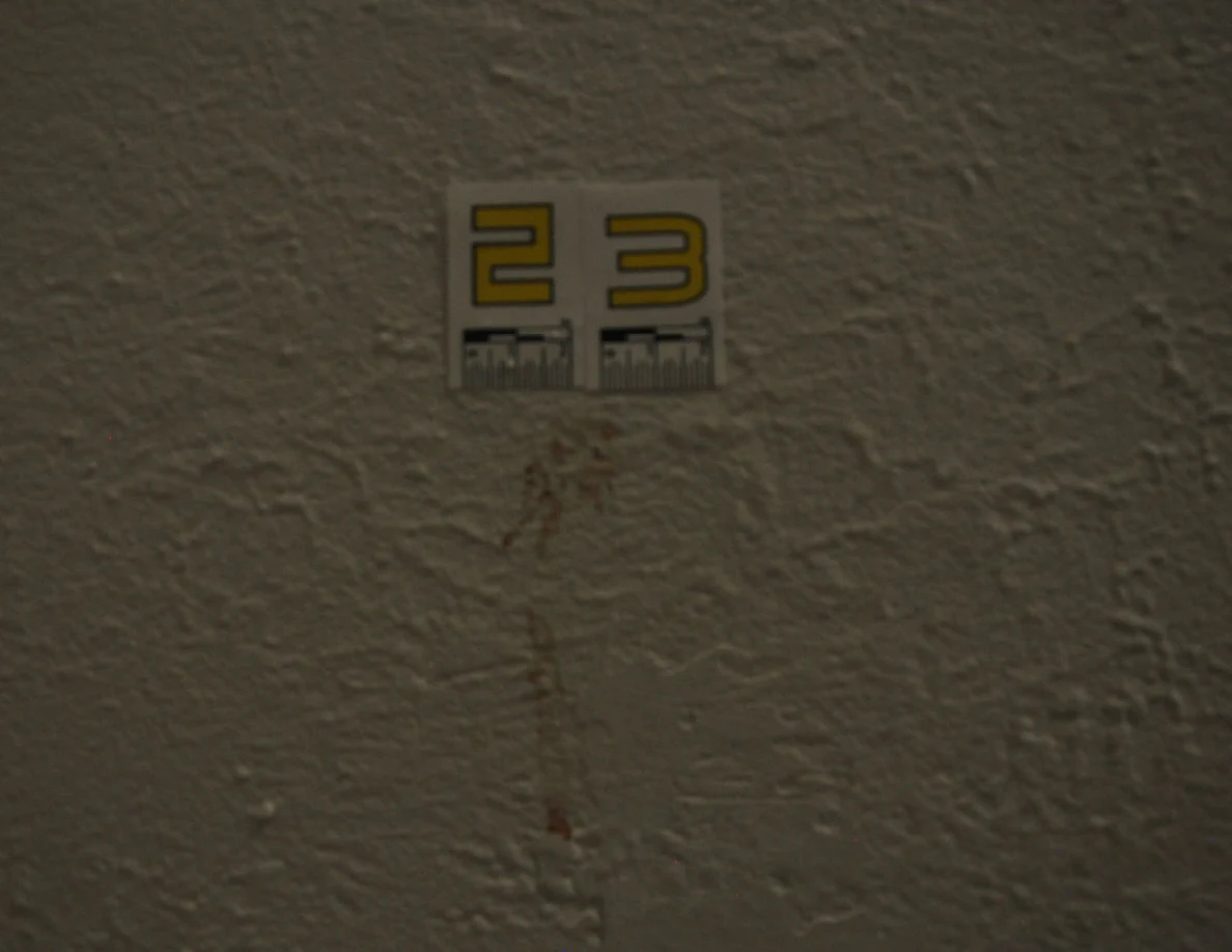 Dim photograph of label 23 and a reddish vertical streak on a pale wall.