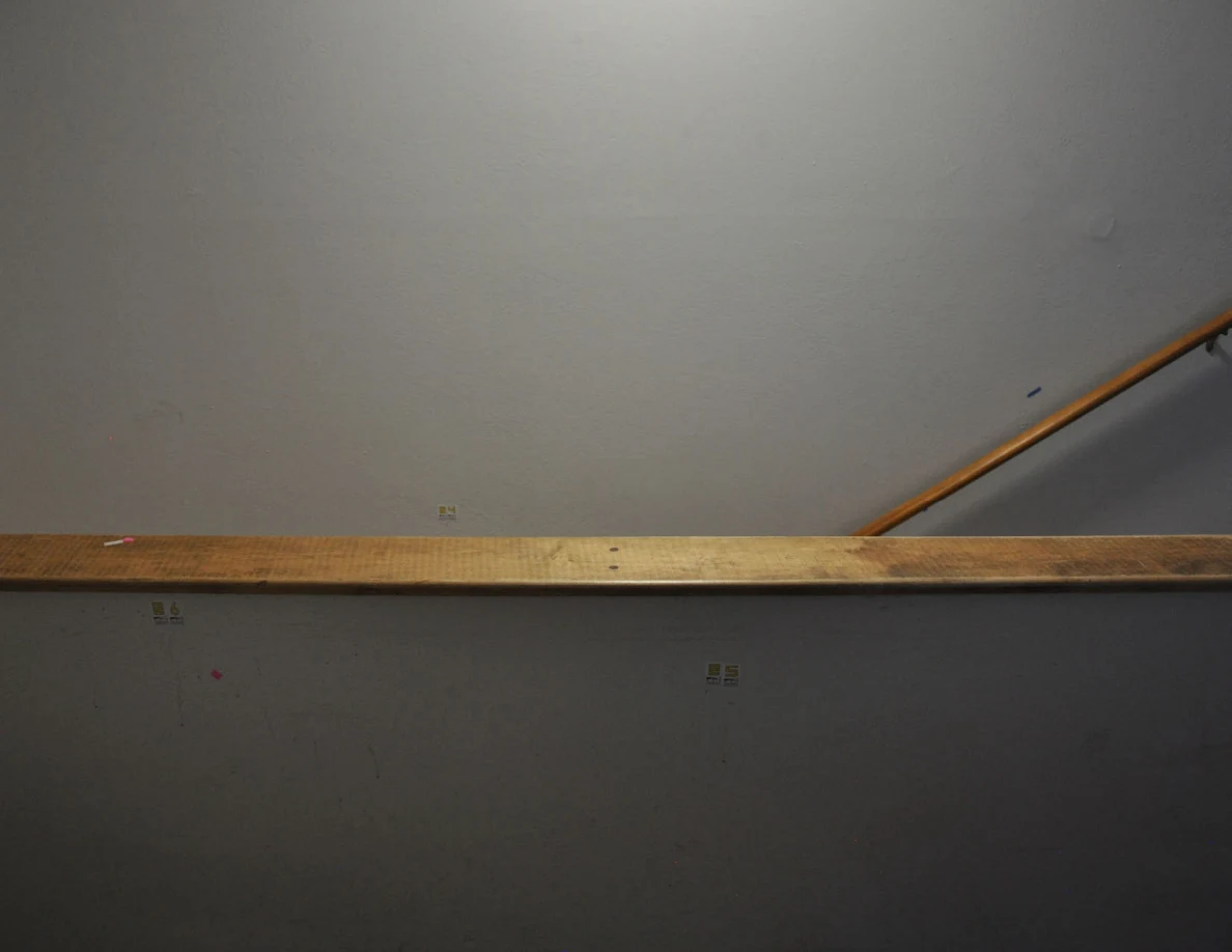 Dim view across a wood-capped stair half-wall toward a wooden handrail and labeled wall.