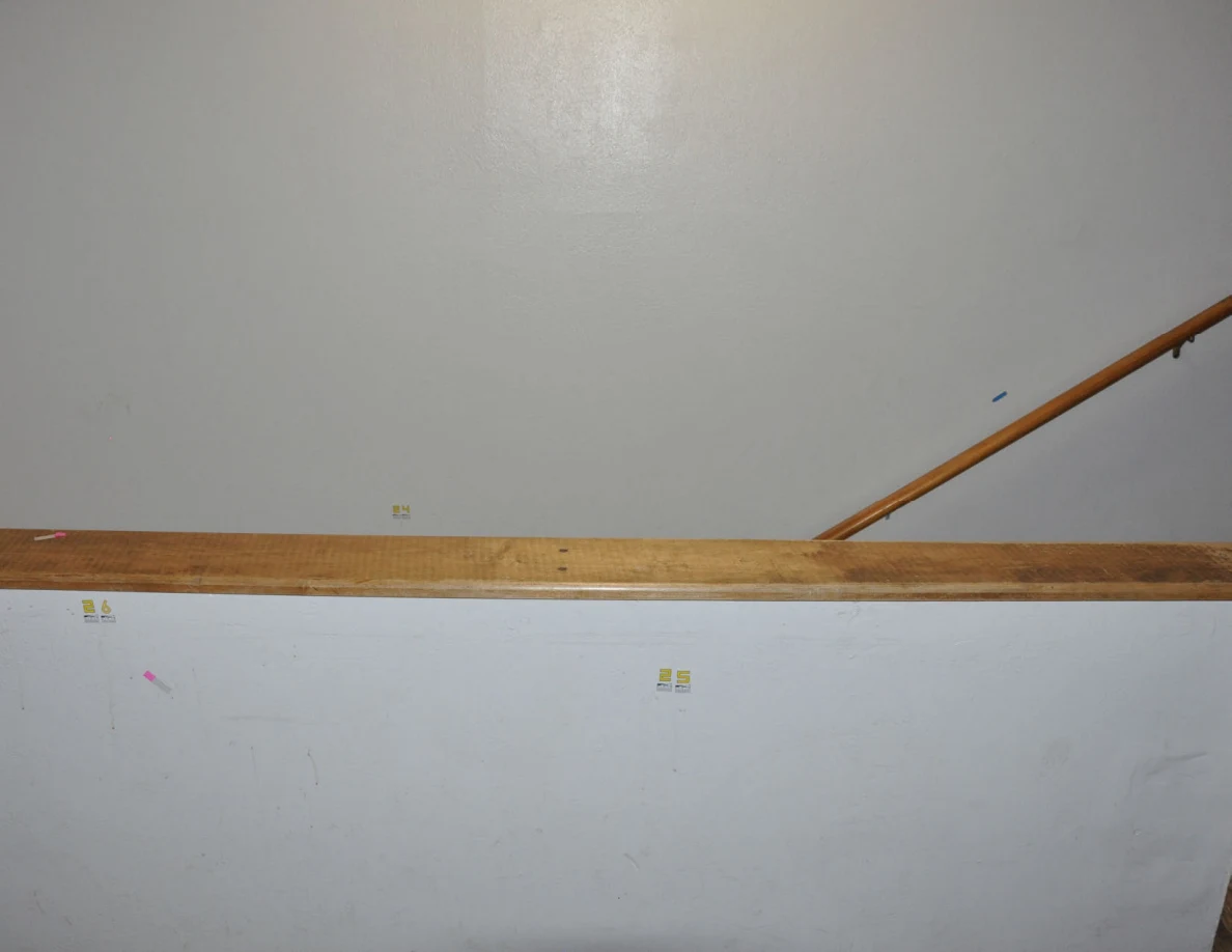 Bright view across a stair half-wall with small yellow labels and a wooden handrail beyond.