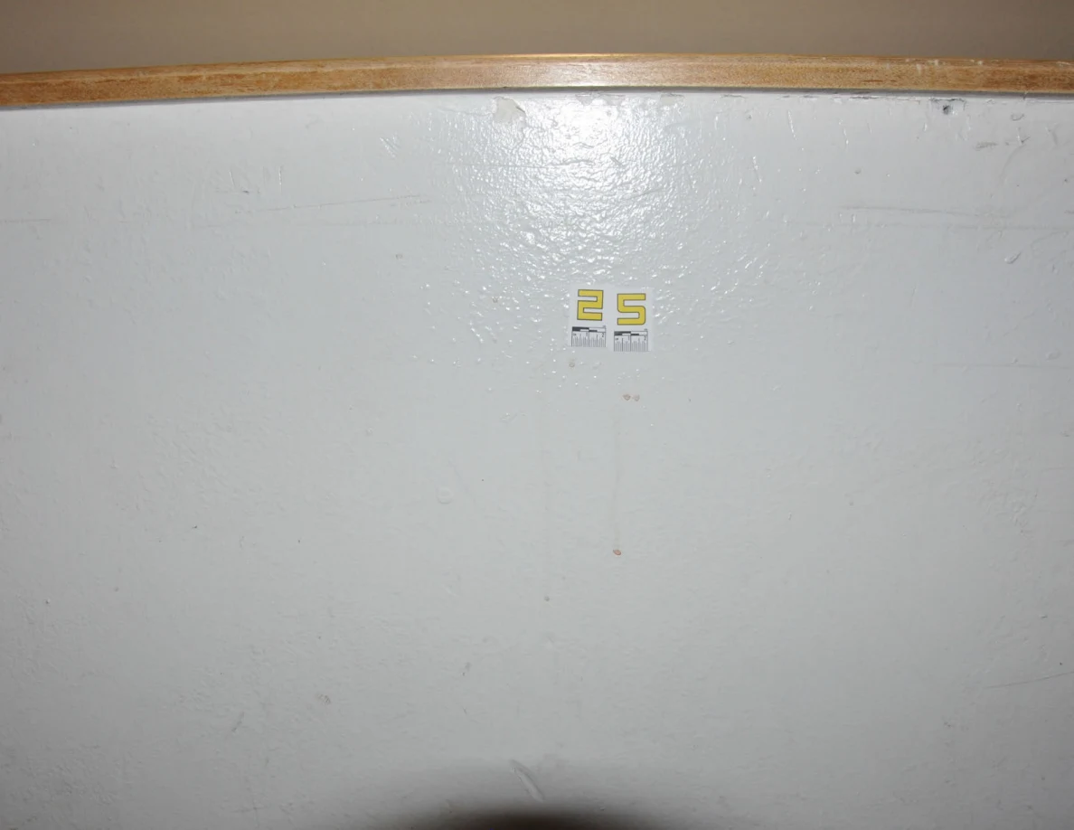 Yellow label 25 beneath a wooden half-wall cap with faint reddish spots below.
