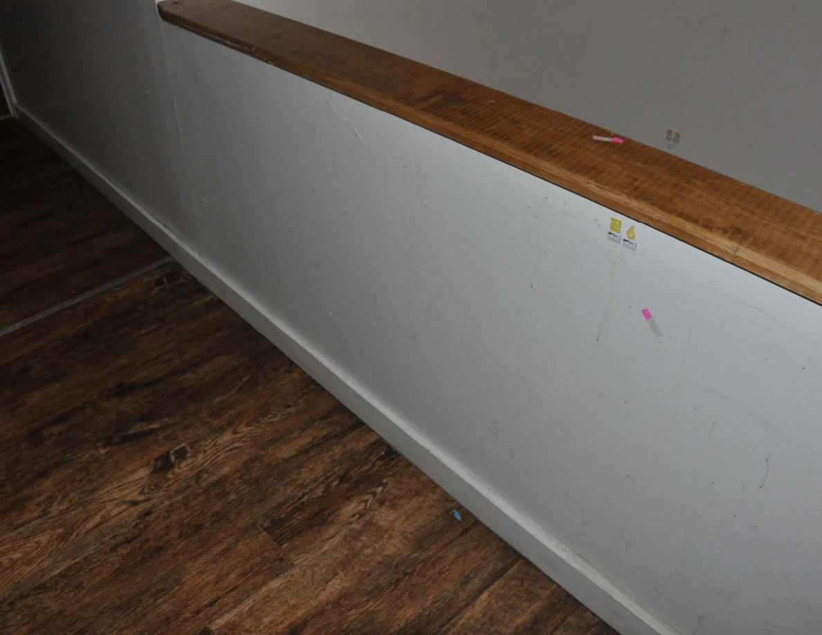 Angled view of a half-wall with label 26 and pink tape beneath the wooden cap.