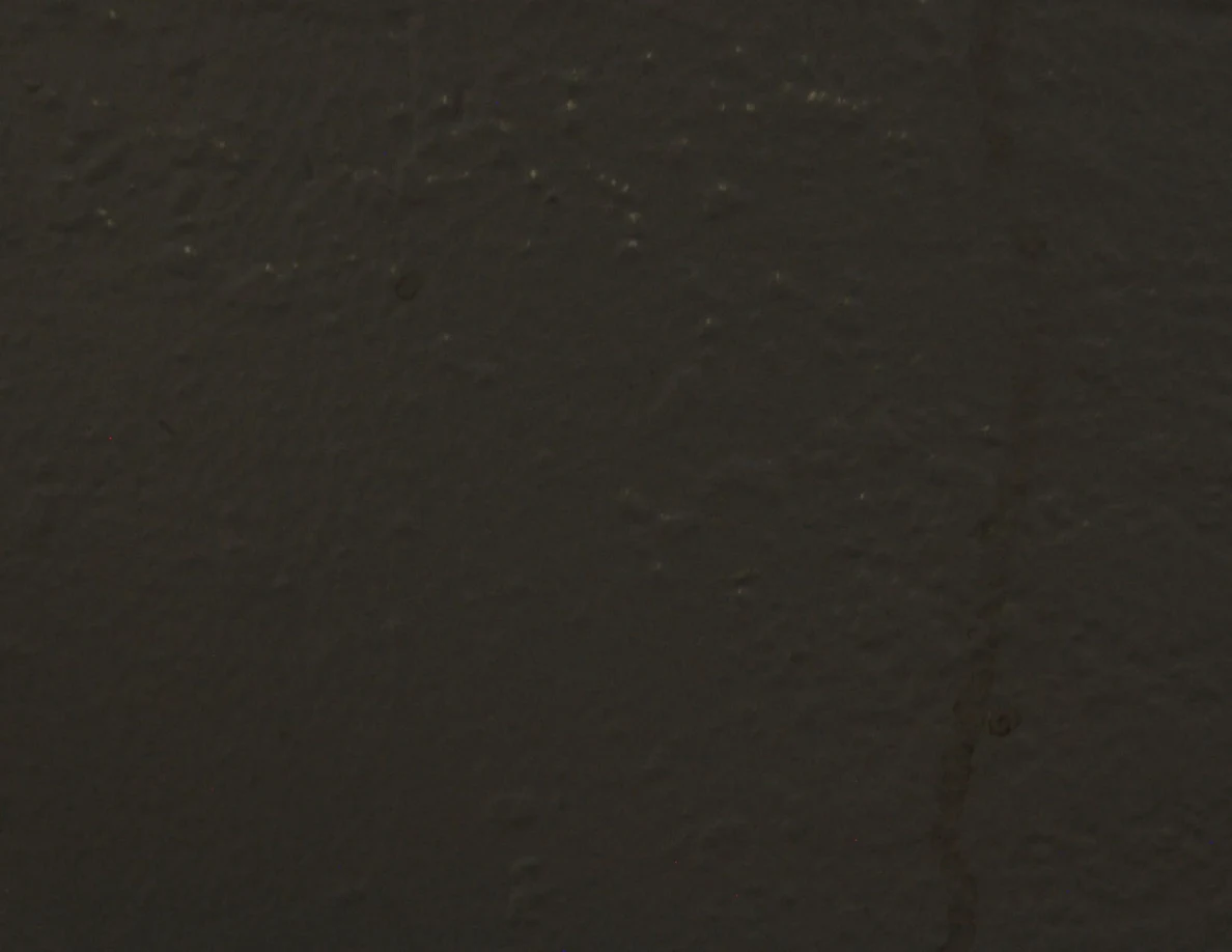 Dim close view of thin reddish streaks on textured wall.