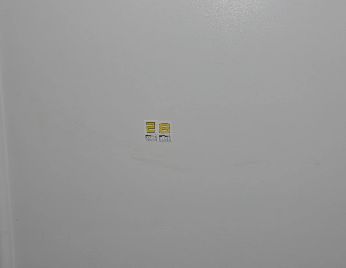 Yellow label 28 above a faint curved scuff on a pale wall.
