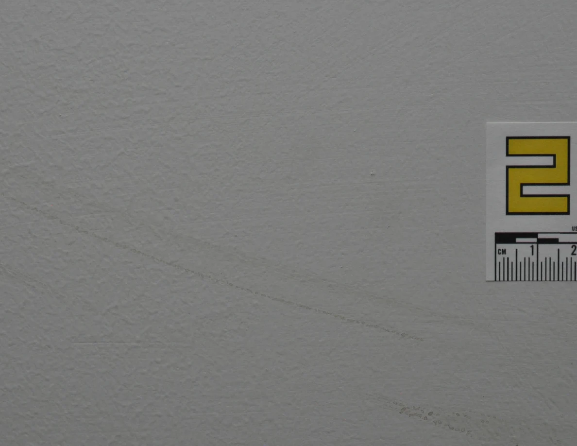 Faint curved wall scuff beside the cropped edge of a yellow label.