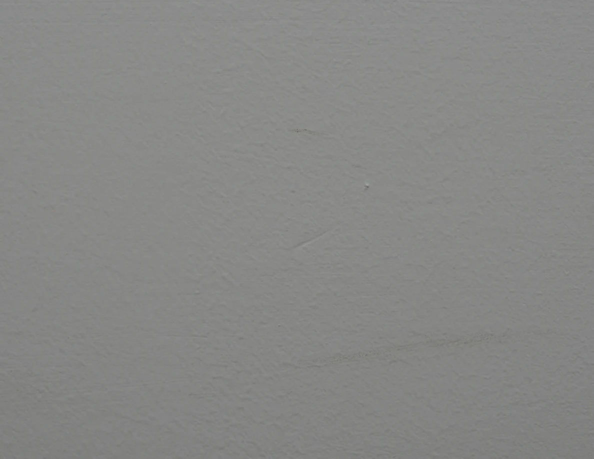 Close view of a faint curved scuff across a pale textured wall.