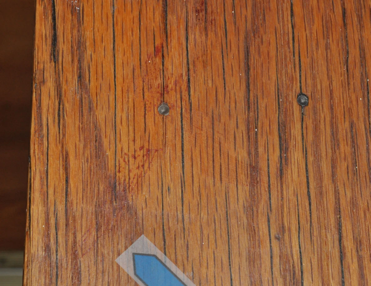 Close view of reddish marks and screw heads on wood grain beside a blue arrow.