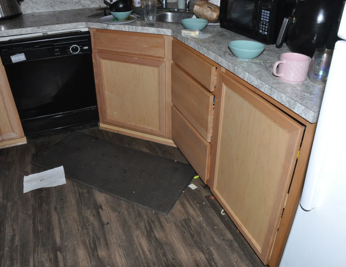 Kitchen cabinets and drawers partly open beside dishwasher, bowls, mugs and countertop appliances.
