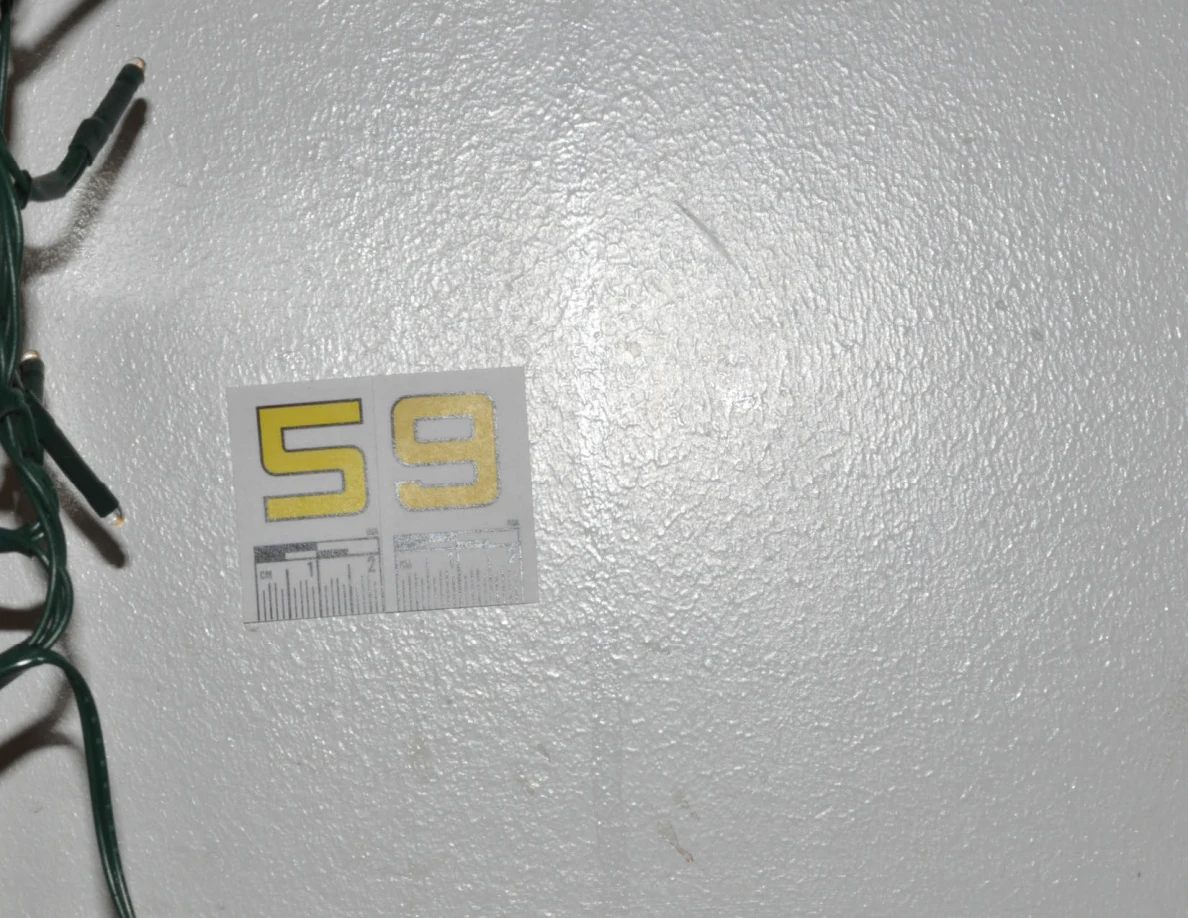 Close view of label 59 and faint marks on a pale wall beside string-light cable.