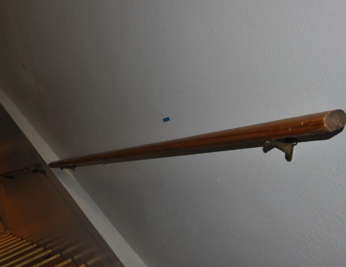 Angled view down a wooden stair handrail with a blue arrow on the wall above.