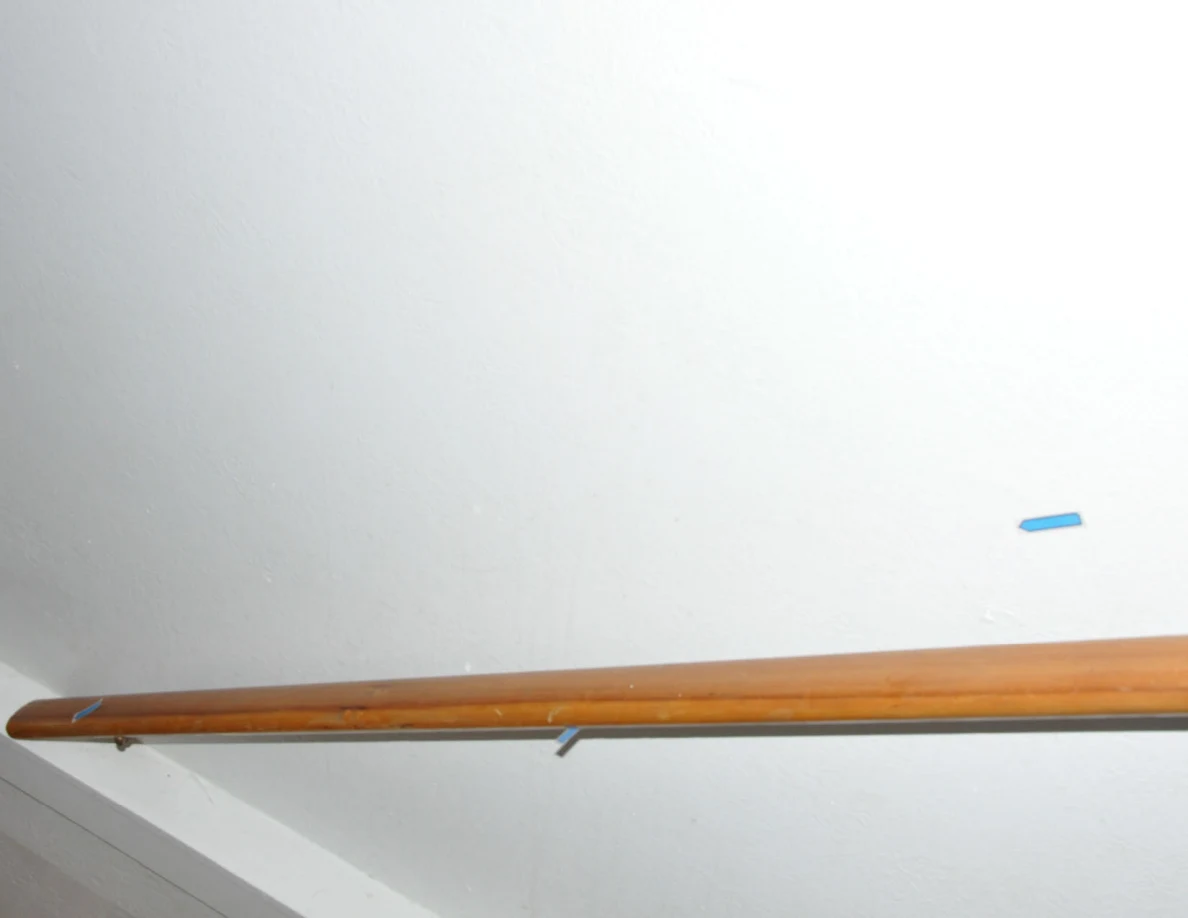 Wooden stair handrail against a pale wall with a blue arrow.